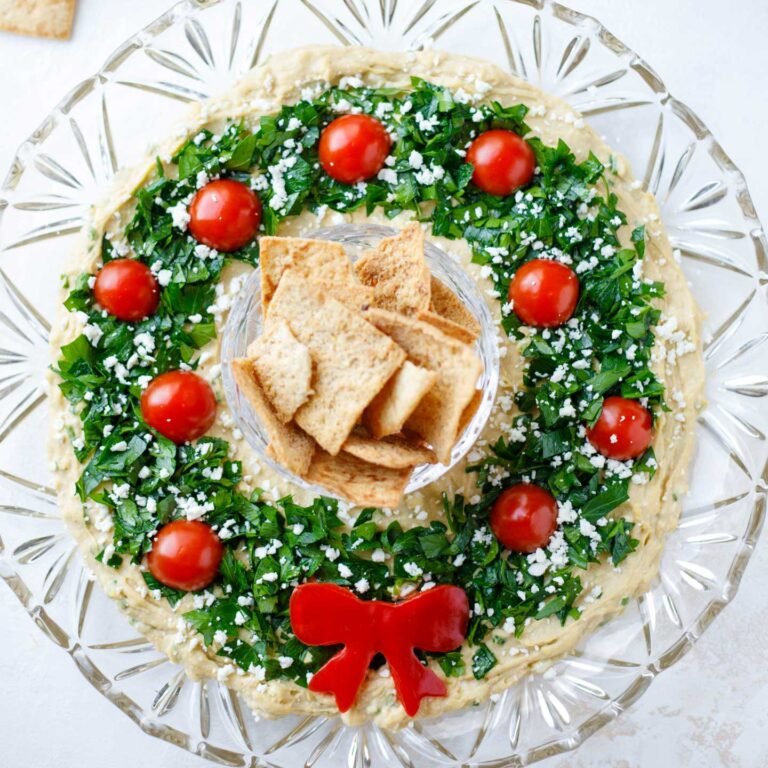 Festive Christmas appetizer hummus wreath with cherry tomatoes, herbs, and pita chips